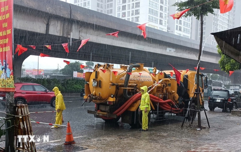 Công nhân ứng trực tiêu thoát nước trong mưa lớn tại đường Nguyễn Xiển. (Ảnh: TTXVN)